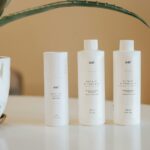 three bottles of lotion sitting on a table next to a potted plant