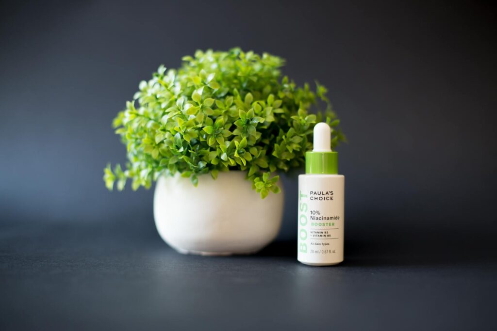 A Serum Beside a White Ceramic Vase with Green Plant