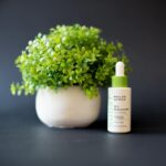 A Serum Beside a White Ceramic Vase with Green Plant